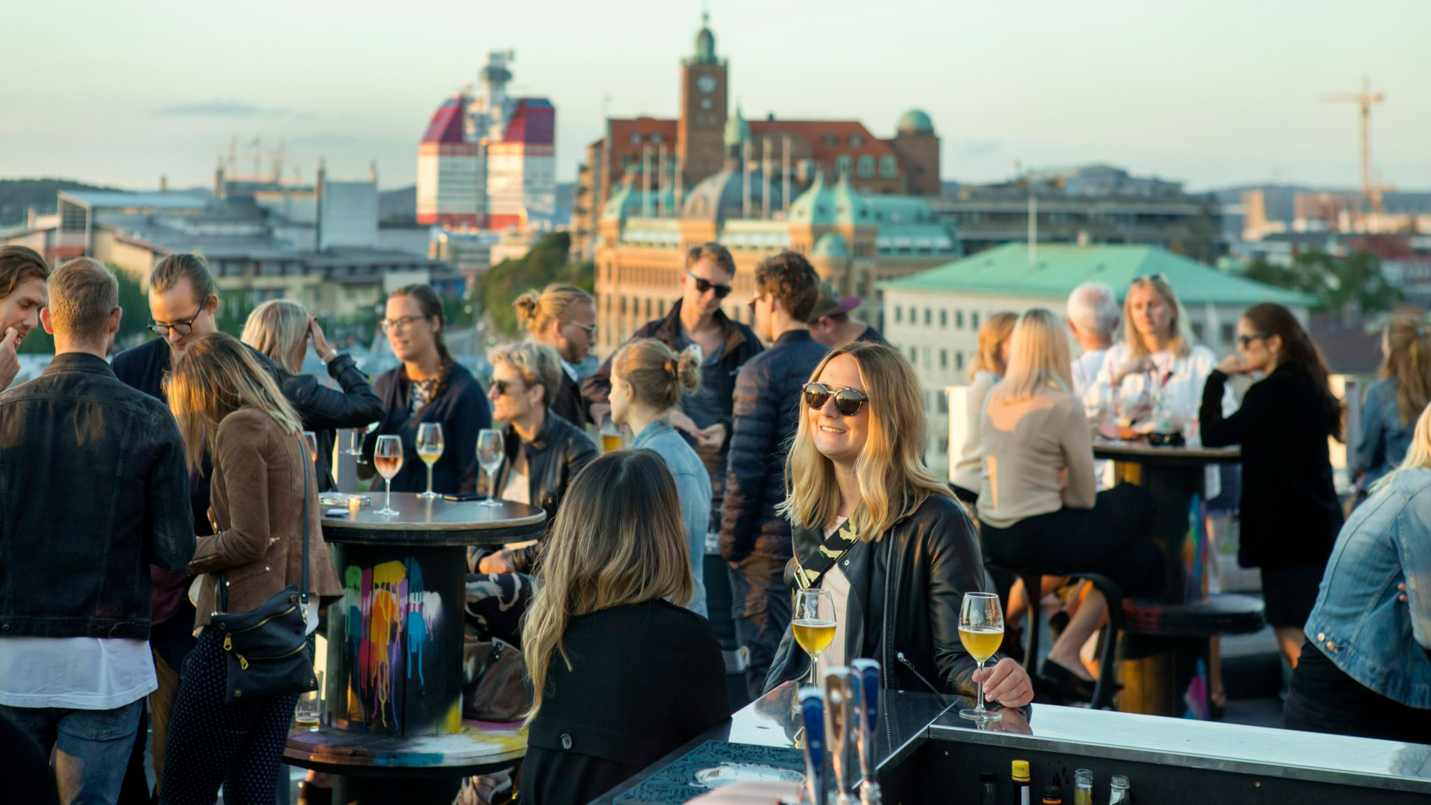 Människor minglar på en takterrass , i bakgrunden ser man byggnaden som kallas Läppstiftet i Göteborg