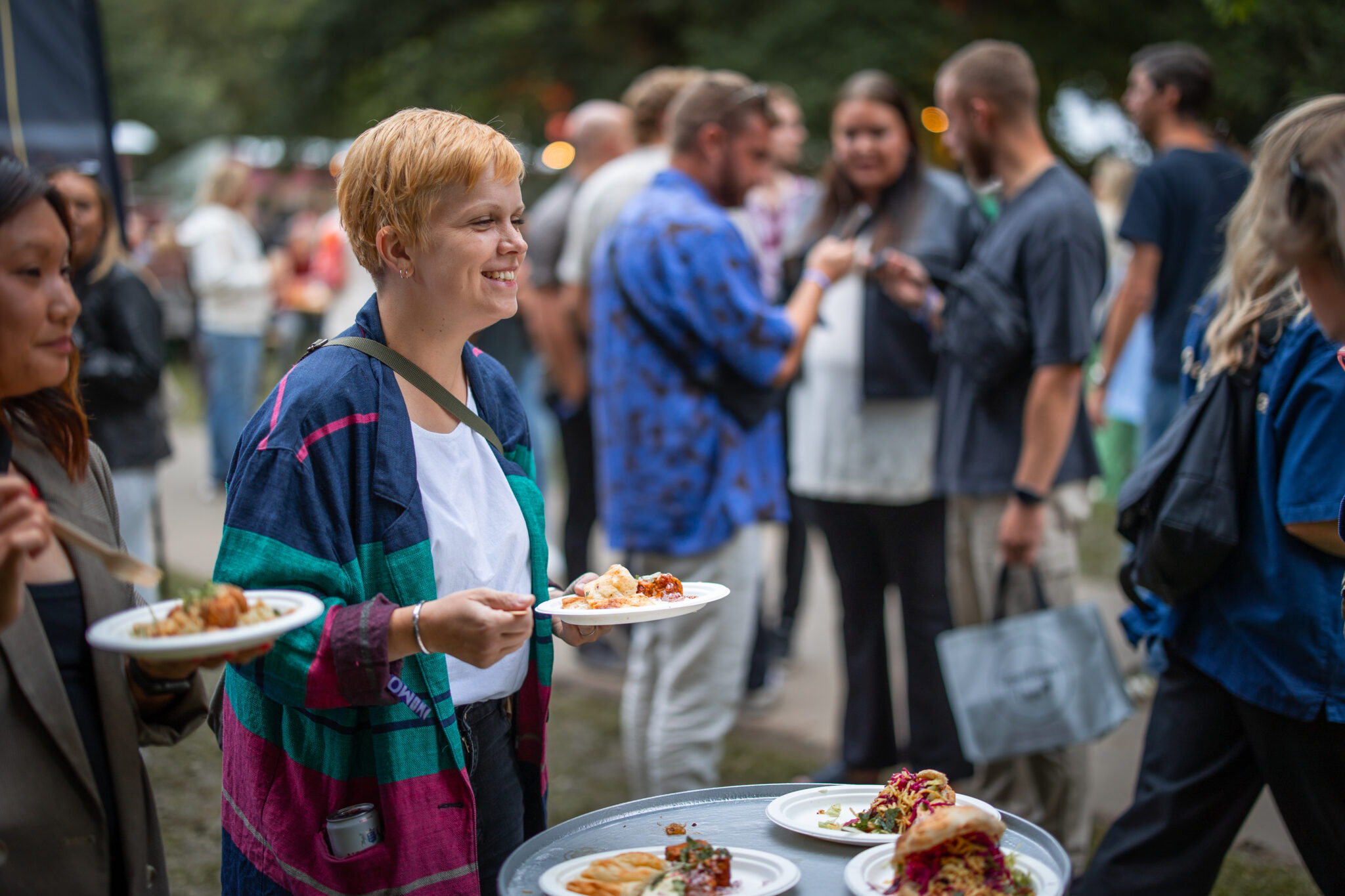 Korthårig, blond kvinna står och äter mat på festivalområdet på Way Out West, i Slottsskogen Göteborg.